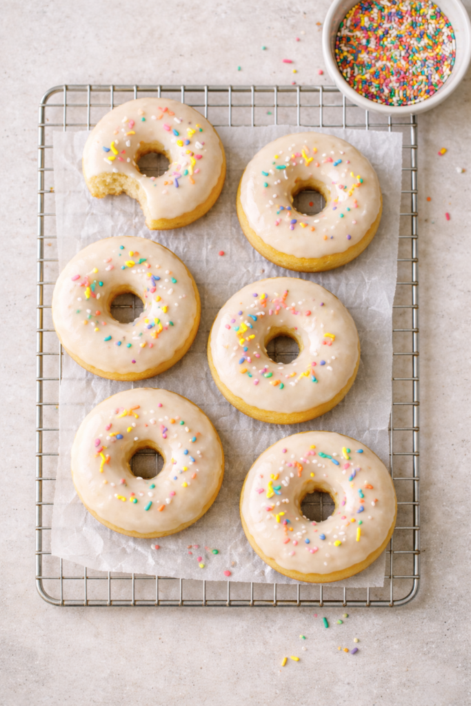 Overhead view of gluten free baked donuts with vanilla glaze and rainbow sprinkles on a cooling rack