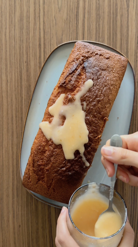 Top-down view of a moist gluten free orange loaf cake being drizzled with a fresh citrus glaze.